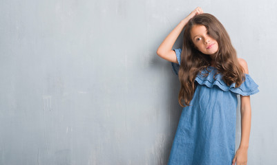 Fototapeta premium Young hispanic kid over grunge grey wall confuse and wonder about question. Uncertain with doubt, thinking with hand on head. Pensive concept.