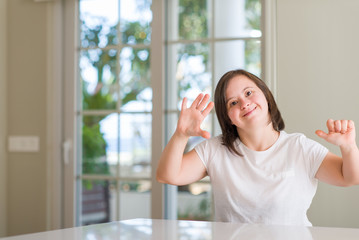 Down syndrome woman at home showing and pointing up with fingers number six while smiling confident and happy.