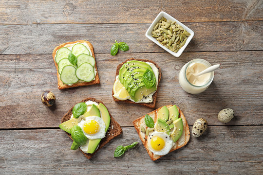 Flat lay composition with toast bread, fried eggs, avocado and cucumber slices on wooden table