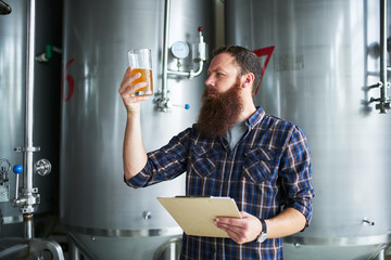 brewer checking beer for qaulity at brewery while holding clipboard