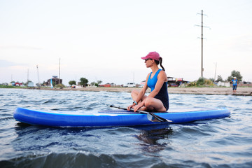 beautiful young girl in sportswear sitting on a SUP board
