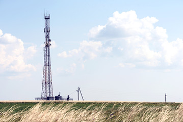 Single large telephone radio communications tomwer in a  grass field with natural sunlight and...