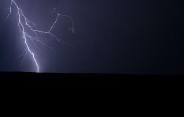 Single lightning strike in nature in a field with colours of white and blue electricity and no...