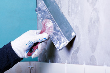 Man hand with trowel plastering a wall, skim coating plaster walls for laying tiles.Construction...