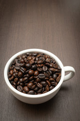roasted coffee beans in cup of coffee on dark wood background