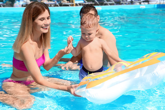 Happy family with little child resting in swimming pool outdoors