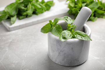 Mortar with fresh green herbs on table
