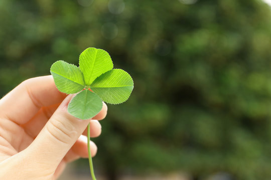 Woman holding four-leaf clover outdoors, closeup with space for text