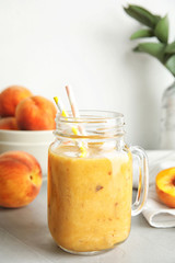 Tasty peach smoothie in mason jar and fresh fruit on table