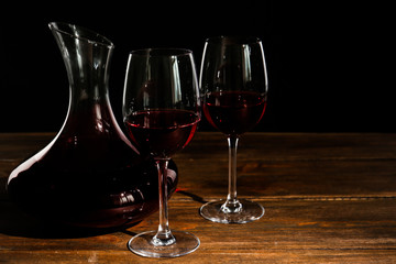 Elegant decanter and glasses with red wine on table against dark background
