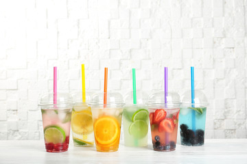 Plastic cups with lemonades on table near white wall