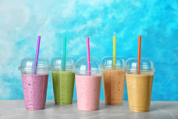 Plastic cups with smoothies on table against color background
