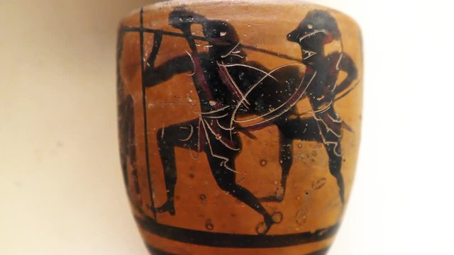 Archeologist inspects tiny ancient authentic Greek vase with mythological masked warriors with spears and shields