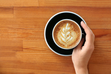Woman with cup of fresh aromatic coffee at wooden table, top view