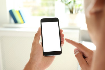 Young man holding mobile phone with blank screen on blurred background, closeup