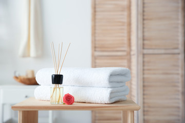 Fototapeta na wymiar Reed air freshener and stack of towels on table against blurred background