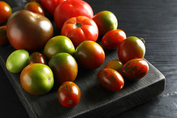 Wooden board with tasty tomatoes on table