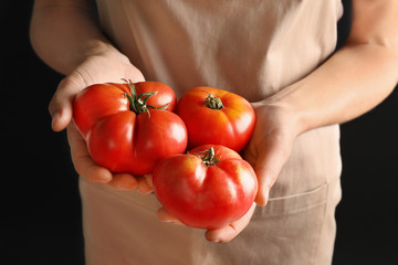 Woman holding tasty juicy tomatoes on black background, closeup