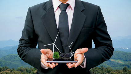 Ecology concept hands holding businessman on a smartphone tree electrical energy clean wind turbine and solar cell the future