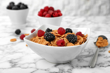 Bowl with cornflakes and berries on marble table. Whole grain cereal for breakfast