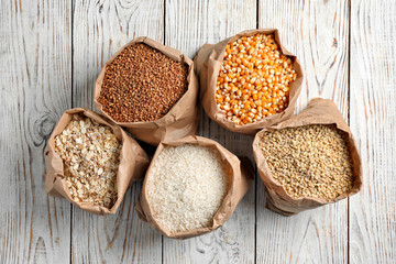 Bags of different cereal grains on wooden background, top view