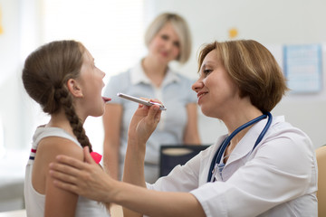 Little girl and her mother at pediatrician office. Doctor examining child's throat