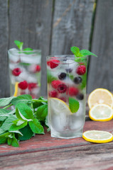 Cold lemonade with lemon, mint and berries in a transparent glass with facets. On an old wooden background