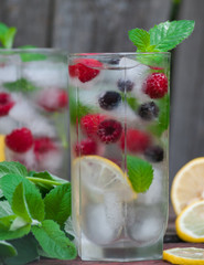 Cold lemonade with lemon, mint and berries in a transparent glass with facets. On an old wooden background