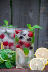 Cold lemonade with lemon, mint and berries in a transparent glass with facets. On an old wooden background