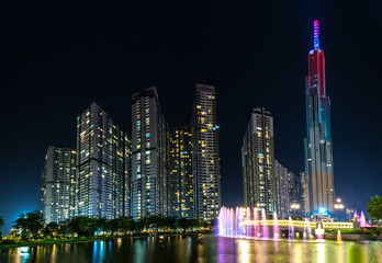 Fototapeta na wymiar Ho Chi Minh City, Vietnam - August 1st, 2018: A state of art fountain at night with colorful lights shimmering, behind the skyscrapers in the urban park development in Ho Chi Minh City. Minh, Vietnam