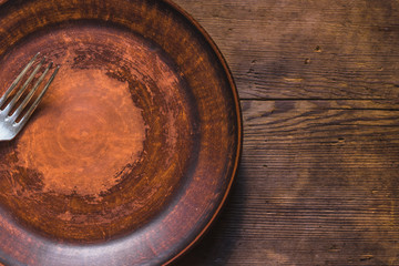 Empty clay plate with a fork on an old wooden table, top view, copy space, close-up