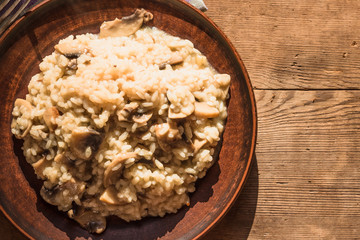 Italian traditional dish - risotto with mushrooms in a clay plate on an old wooden table, top view, copy space for a recipe