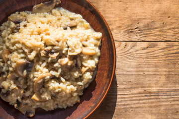 Italian traditional dish - risotto with mushrooms in a clay plate on an old wooden table, top view, copy space for a recipe