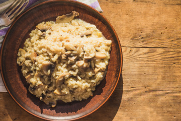 Italian traditional dish - risotto with mushrooms in a clay plate on an old wooden table, top view, copy space for a recipe