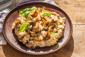 Italian traditional dish - risotto with mushrooms with basil leaves in a clay plate on an old...