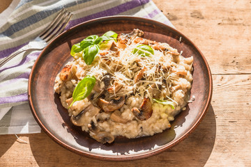 Italian traditional dish - risotto with mushrooms with basil leaves in a clay plate on an old wooden table, top view, copy space for a recipe