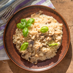 Italian traditional dish - risotto with mushrooms with basil leaves in a clay plate on an old wooden table, top view, copy space for a recipe