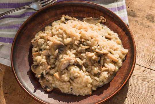 Italian traditional dish - risotto with mushrooms in a clay plate on an old wooden table, top view, copy space for a recipe