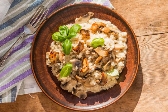 Italian traditional dish - risotto with mushrooms with basil leaves in a clay plate on an old wooden table, top view, copy space for a recipe