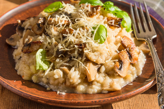 Italian dish - vegetarian mushroom risotto with basil leaves and Parmesan cheese in a clay plate naprostovatom village table