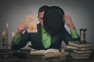 Man hiding his face behind a bowler hat and showing a top secret documents in hands. Detective or spy agent or police inspector concept.