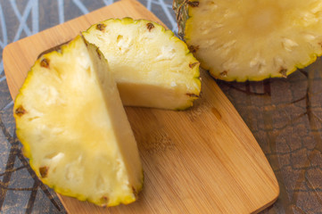 Two pieces of pineapple sliced on a board kept on a table with copy space