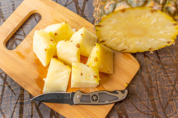 Top view of Pineapple slices kept on a chopping board with a knife and chopped sliced pineapple with copy space