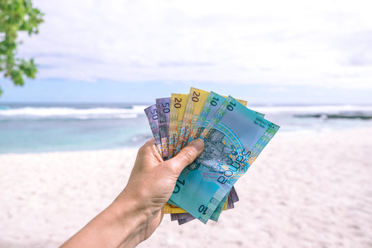Samoan Tala currency - left hand holding bank notes from Western Samoa against backdrop of South Pacific ocean and beach