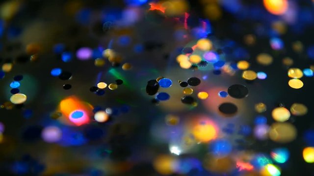 Defocused shimmering multicolored glitter confetti, black background. Party, magic, imagination. Rainbow colors, sparkle circles. Holiday abstract festive texture of shiny blurred bokeh light spots.