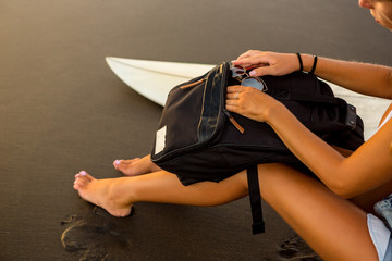 Close up of a young surfer woman in sexy bikini with surf board and travel backpack at sunset...
