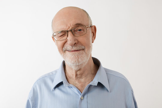 Positive human emotions, feelings and body language. Picture of funny elderly retired man with gray stubble winking at camera. Senior male in eyeglasses blinking at you, having playful look