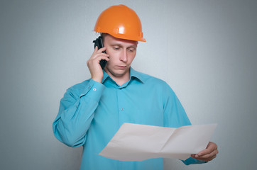 Builder construction worker with mobile phone is holding in hand a plan draft document isolated on gray background.