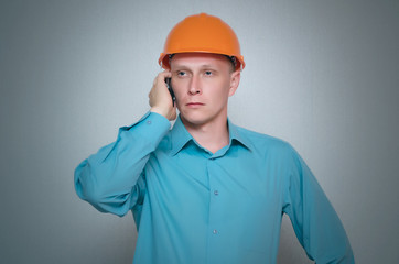 Builder worker is talking on mobile phone isolated on gray background.