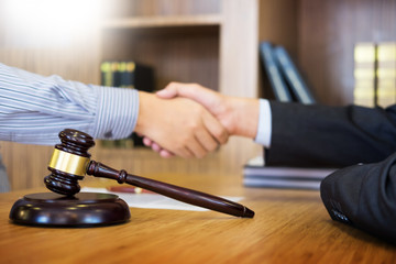 Gavel Justice hammer on wooden table with judge and client shaking hands after adviced in background at courtroom, lawyer service concept.